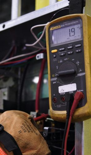 Electrician using a multimeter to fix industrial control panel wiring.