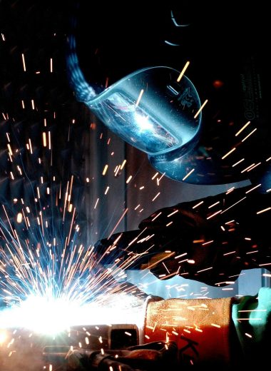 A focused welder works with metal in an industrial setting, creating vibrant sparks.